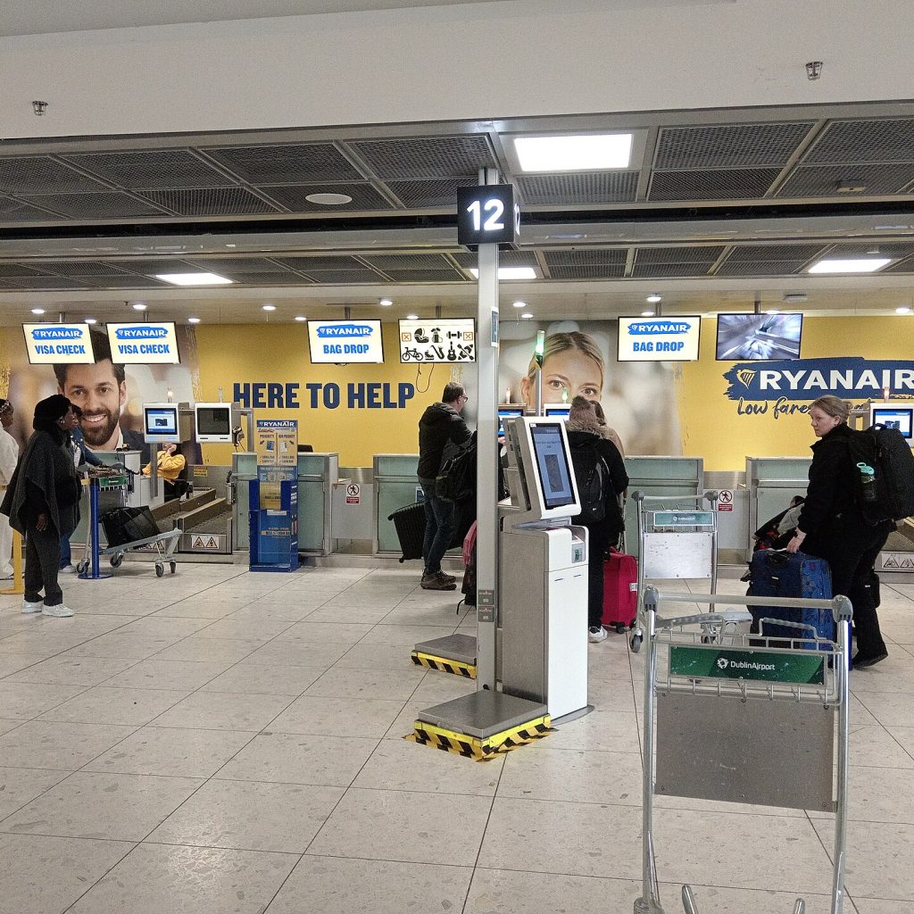 Odbavovací přepážky Ryanair a bag drop v odletové hale letiště s cestujícími a zavazadlovým vozíkem