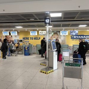 Odbavovací přepážky Ryanair a bag drop v odletové hale letiště s cestujícími a zavazadlovým vozíkem