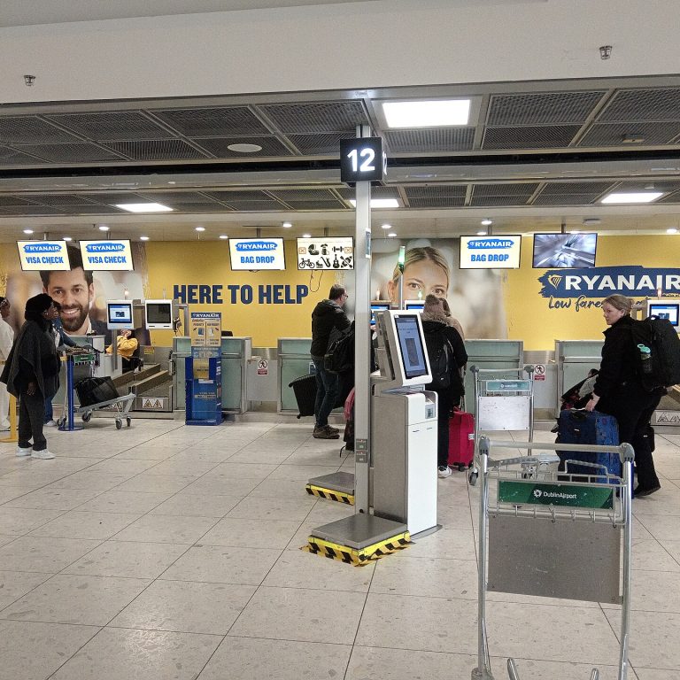 Odbavovací přepážky Ryanair a bag drop v odletové hale letiště s cestujícími a zavazadlovým vozíkem
